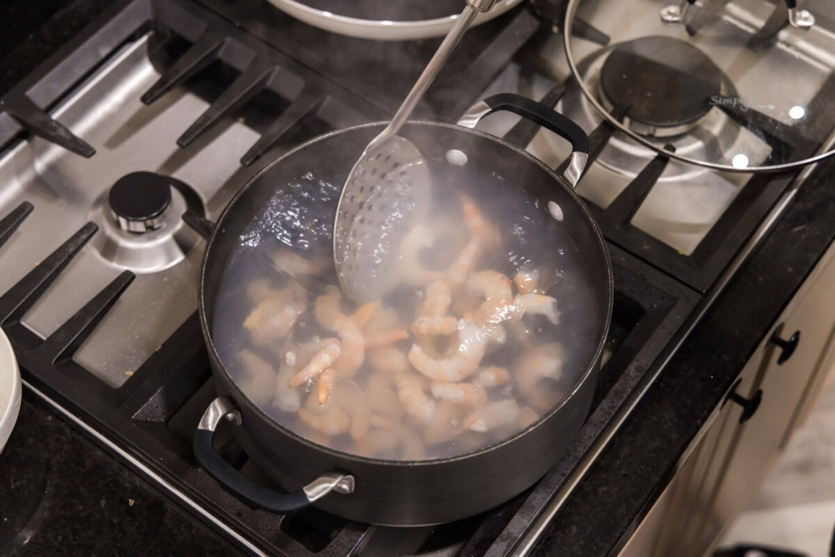 removing shrimp from hot water with a slotted spoon