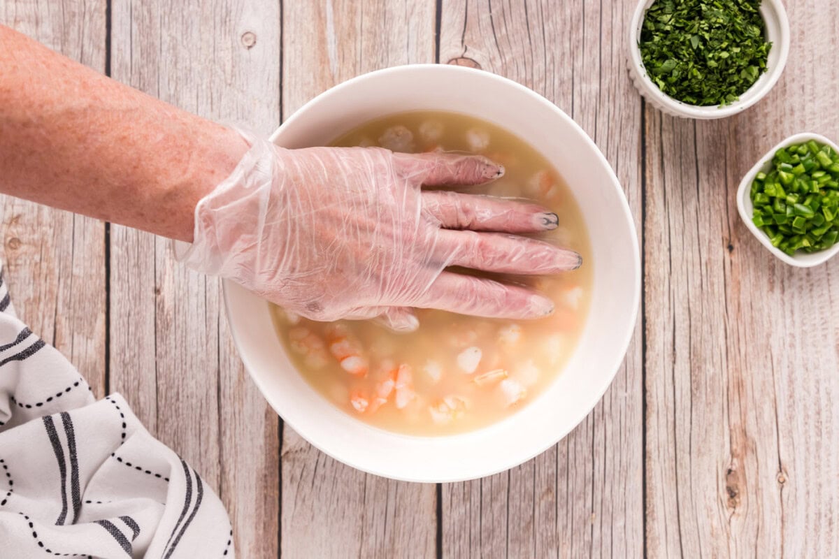 hand pressing down on shrimp in a bowl with citrus juice