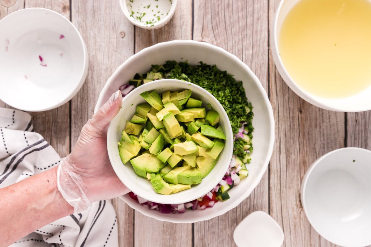 adding avocado to bowl of diced fruits and vegetables with shrimp