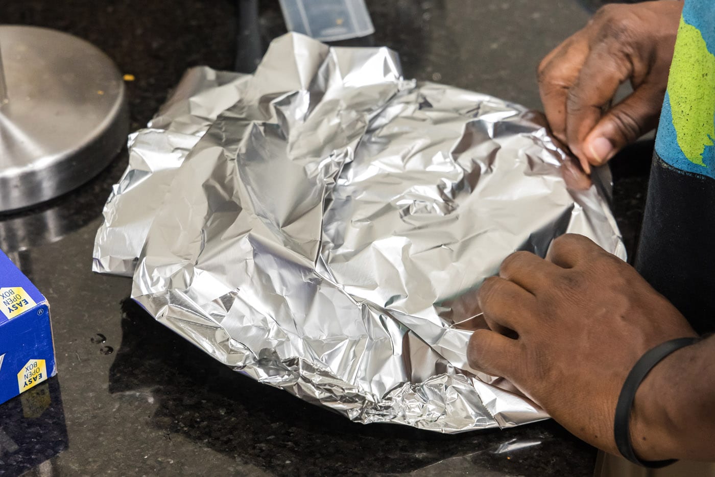 hands folding foil over cooked ribeye steaks