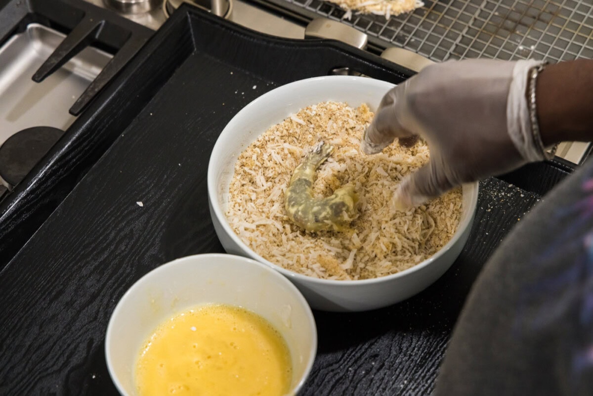 hand dipping dredged shrimp into coconut and panko mixture