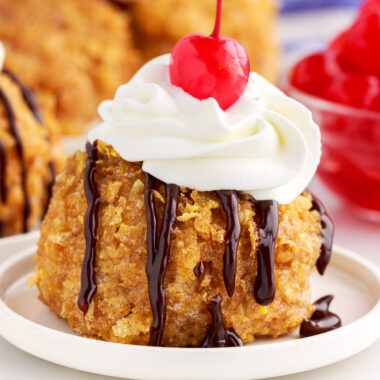 Close up of Fried Ice Cream on a plate with chocolate sauce, whipped cream and a cherry on top.