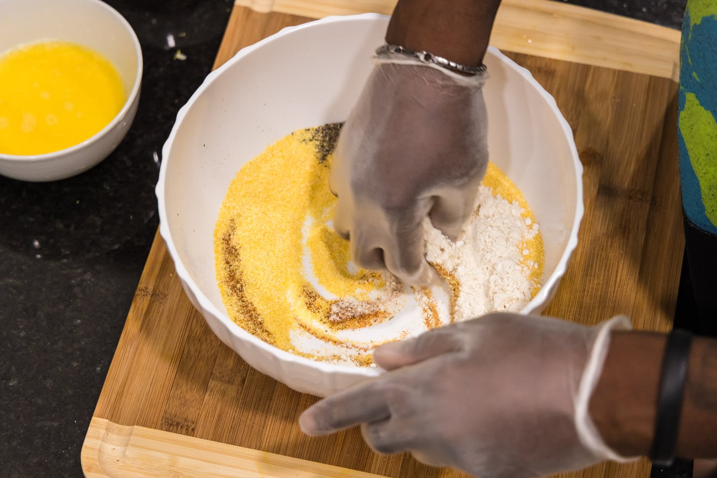 hand mixing spices, seasonings, and flour in a bowl with cornmeal