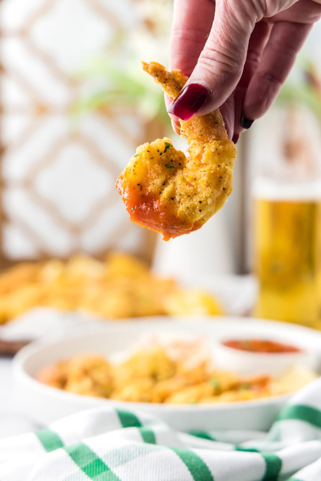 A hand holding a Fried Shrimp dipped in cocktail sauce