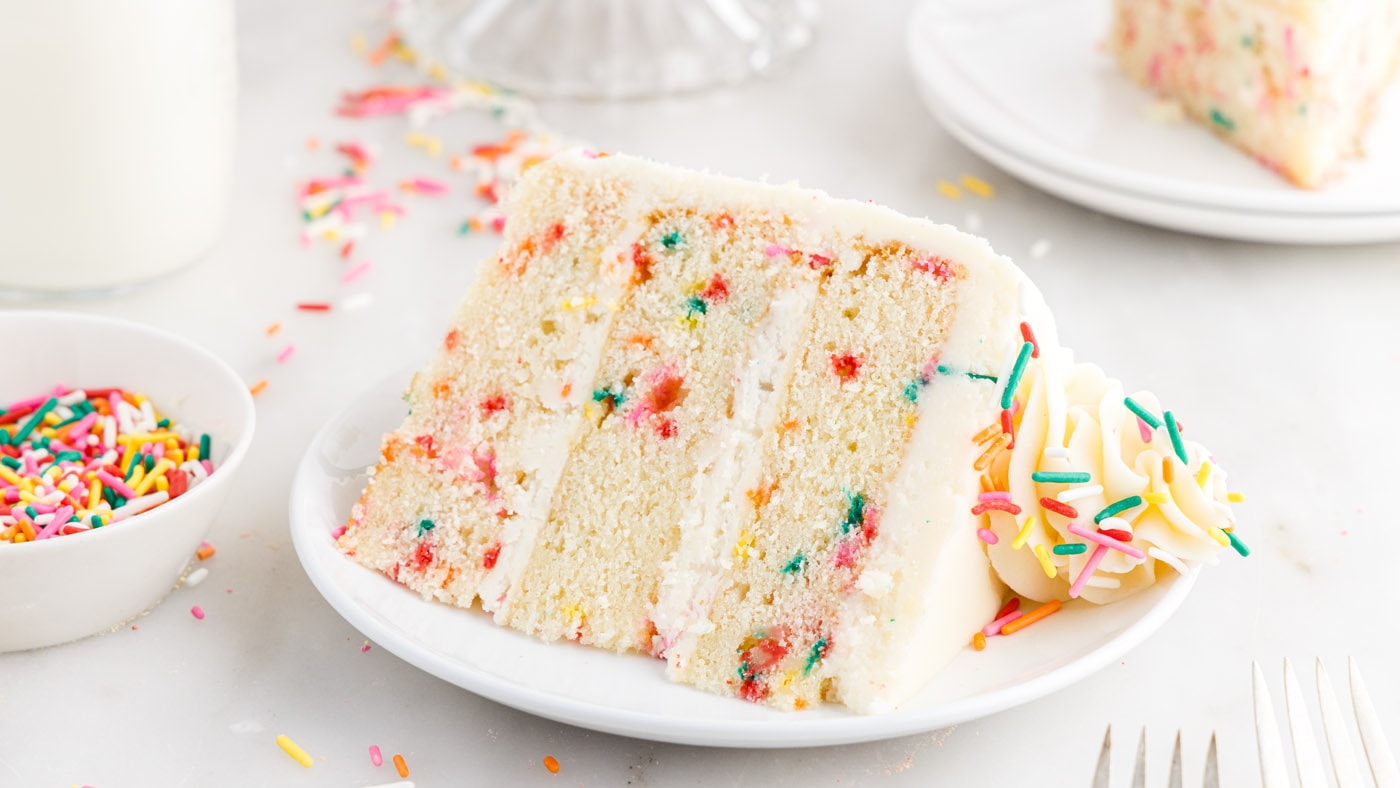 An explosion of colorful sprinkles meets a three-tiered vanilla cake with a soft, dense crumb. Every