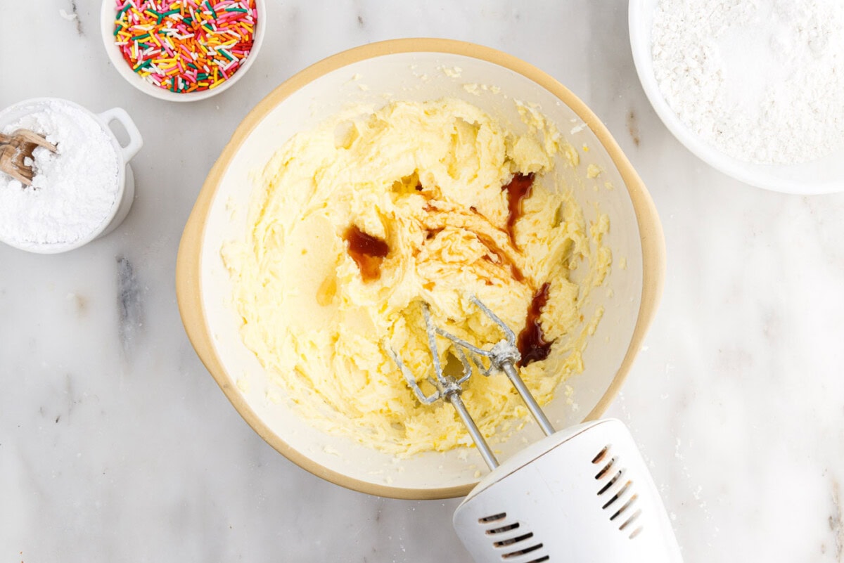 beating vanilla, almond, and oil into butter and sugar mixture in a bowl