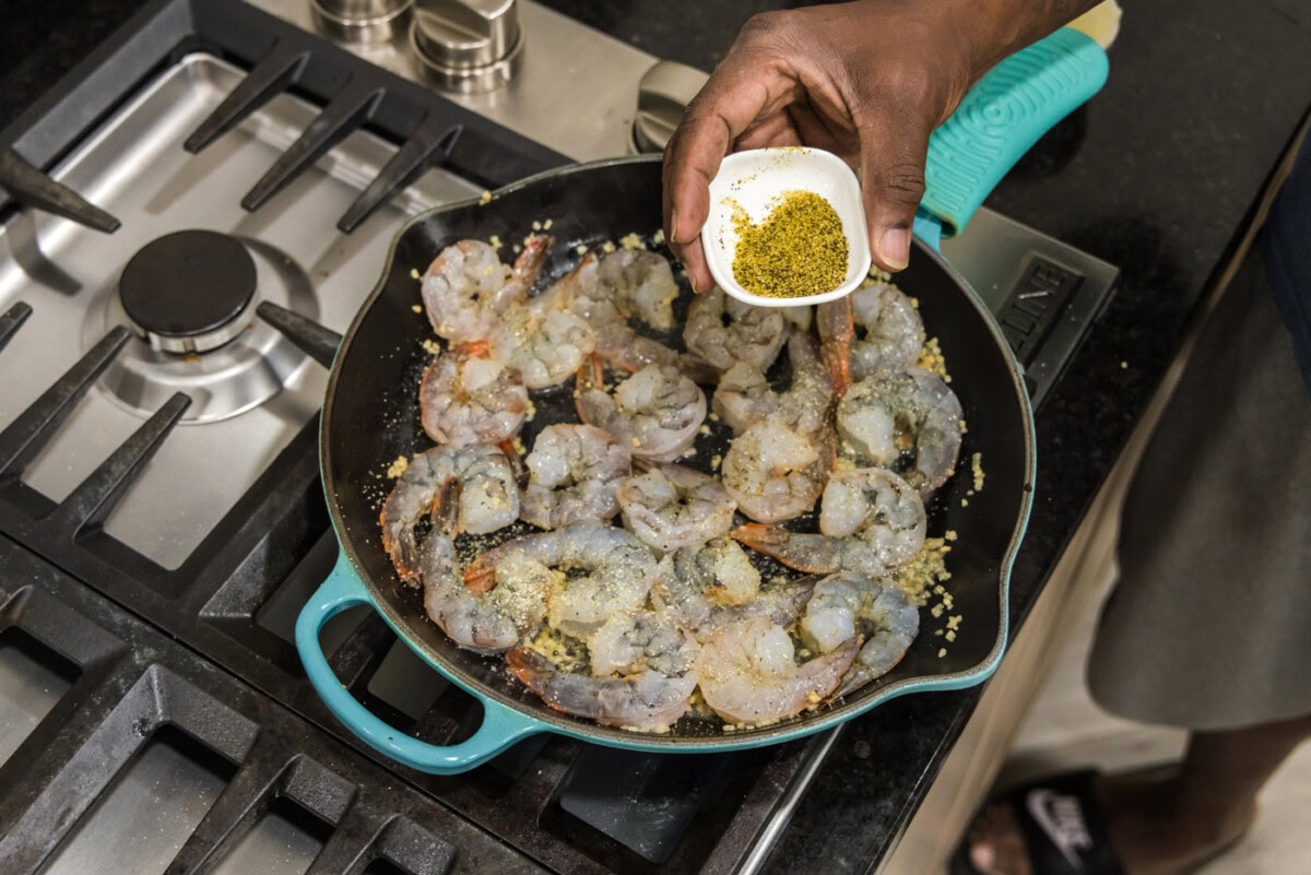 adding lemon pepper to shrimp in a skillet