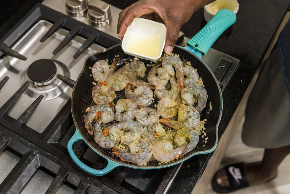 adding lemon juice to skillet with seasoned shrimp and butter