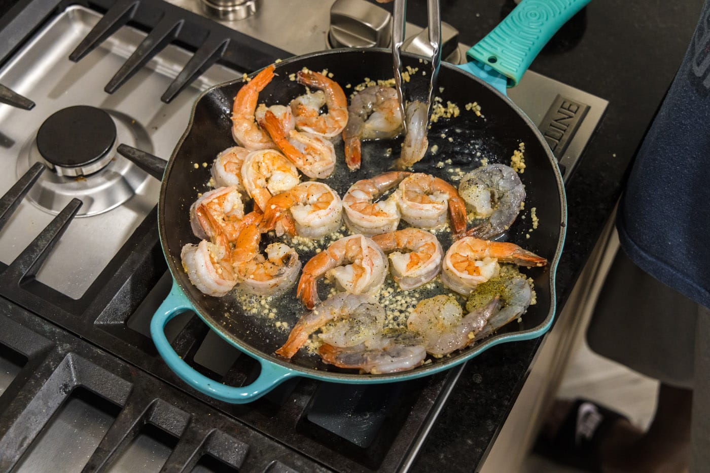 tongs flipping shrimp over in a skillet