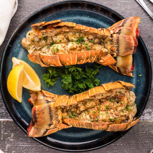 Overhead photo of two Grilled Lobster Tails on a plate with lemons