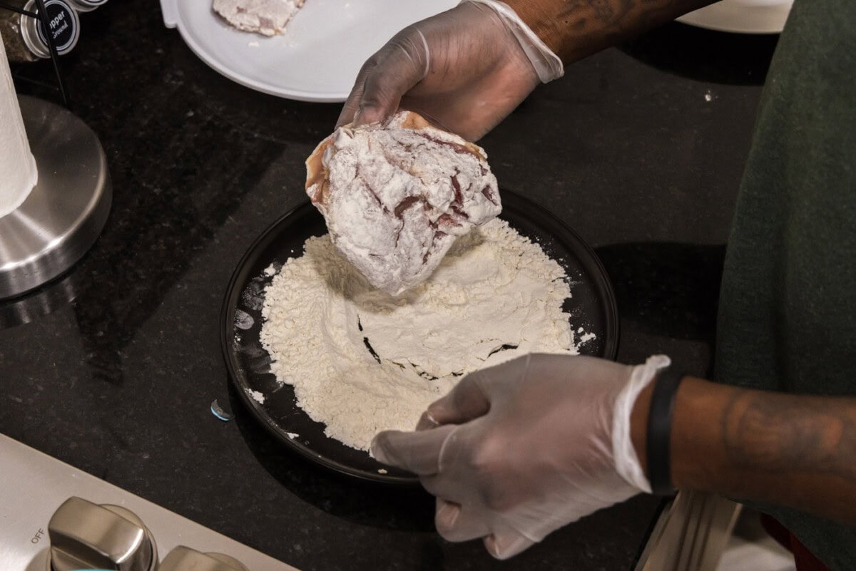 hand dredging chicken thigh in flour