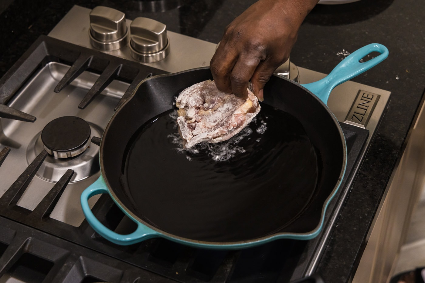 placing floured chicken thigh in skillet with oil