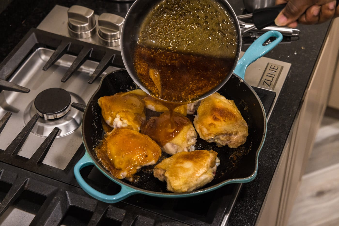 pouring honey garlic sauce over chicken thighs in a skillet