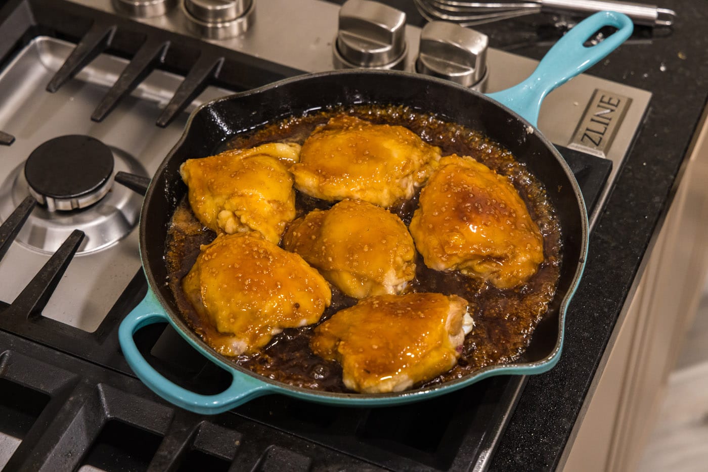 chicken thighs cooking in a skillet with honey garlic sauce