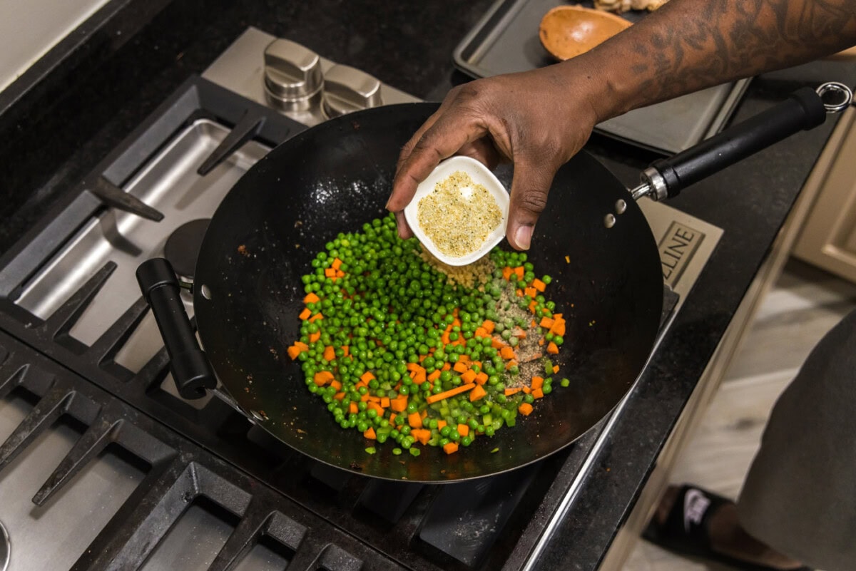 hand adding seasonings to fried rice ingredients