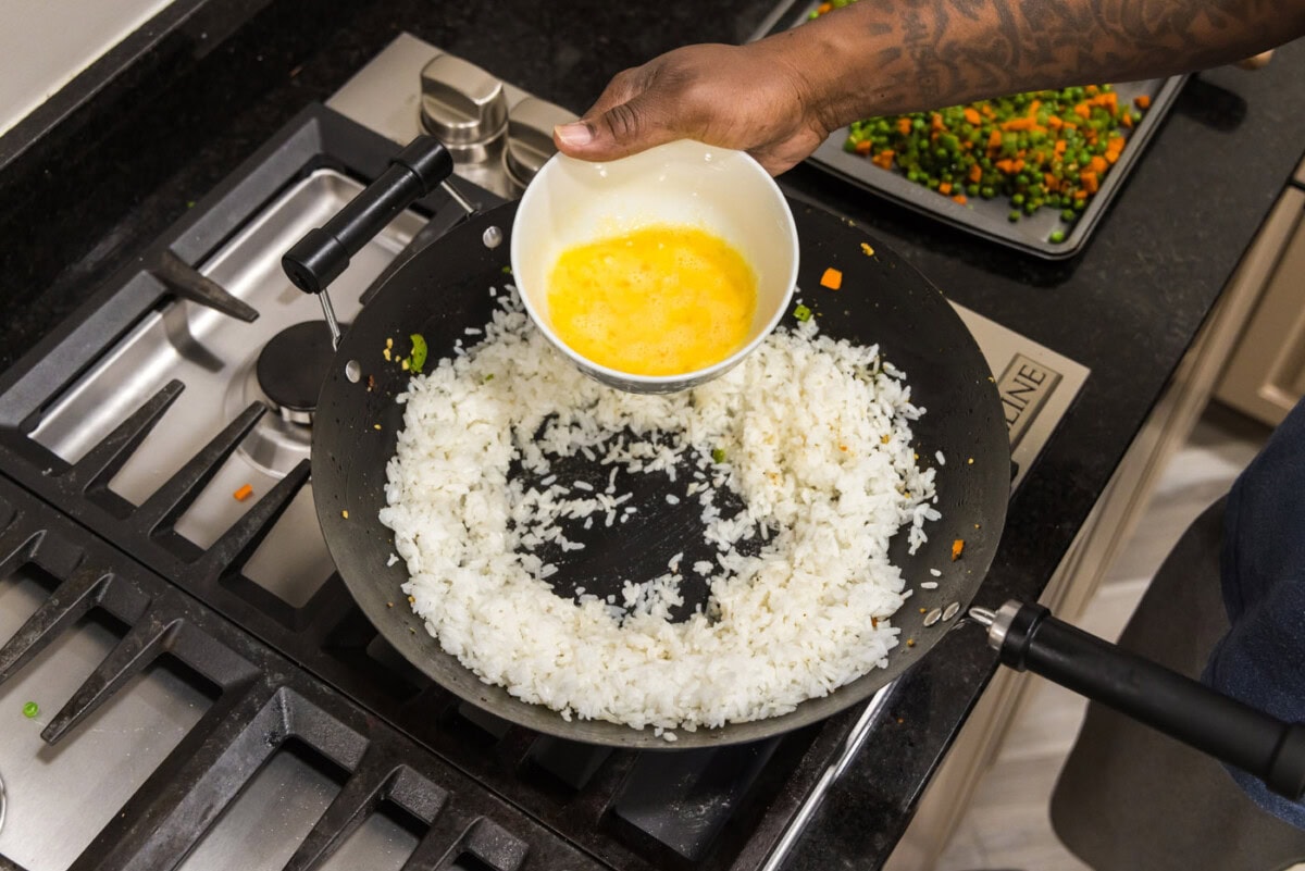 pouring whisked eggs into a well of rice
