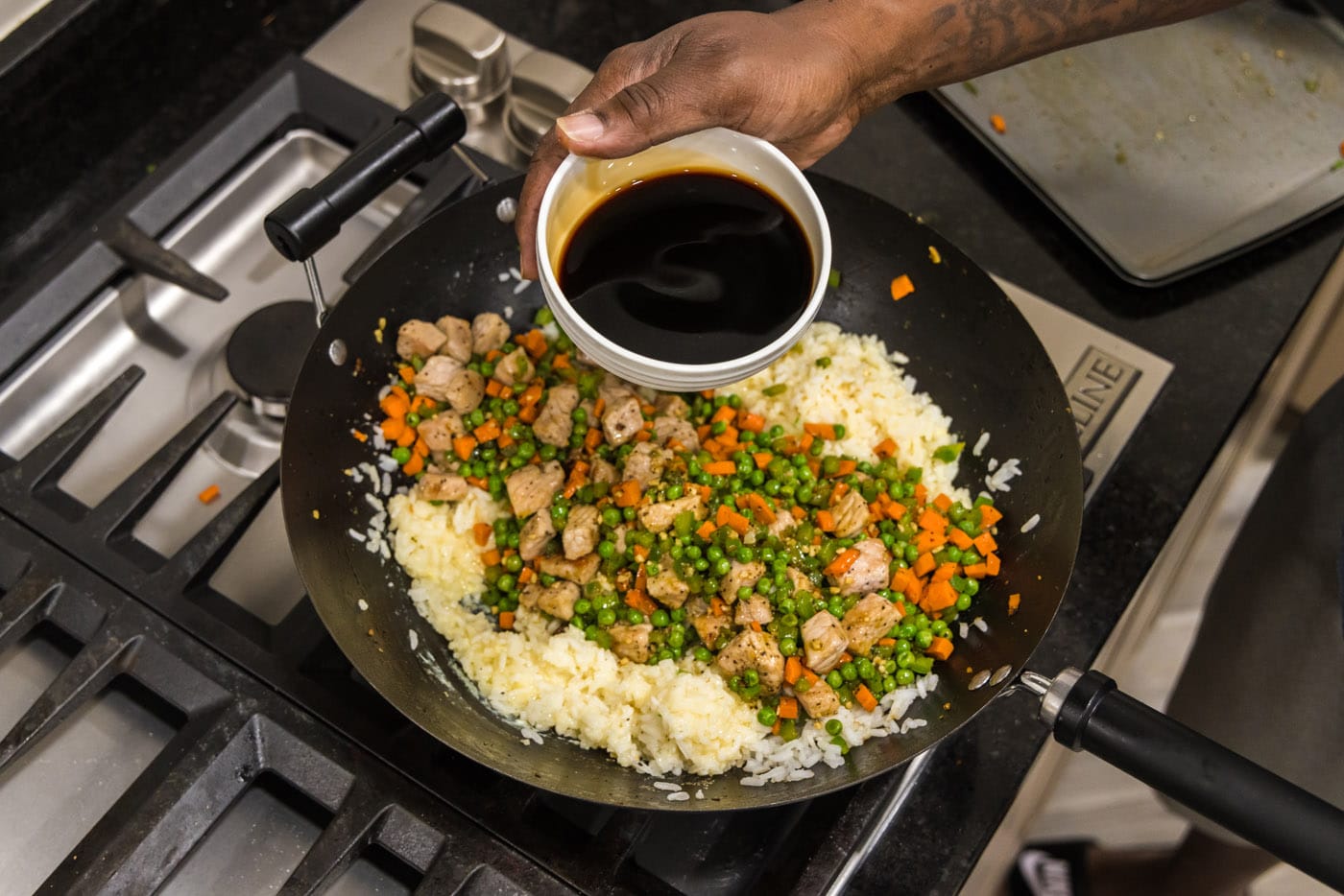Pouring soy sauce into skillet with pork fried rice