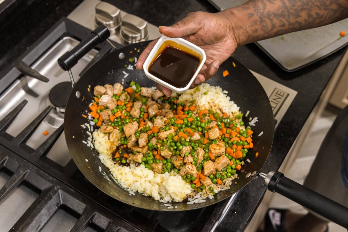pouring oyster sauce into skillet with fried rice