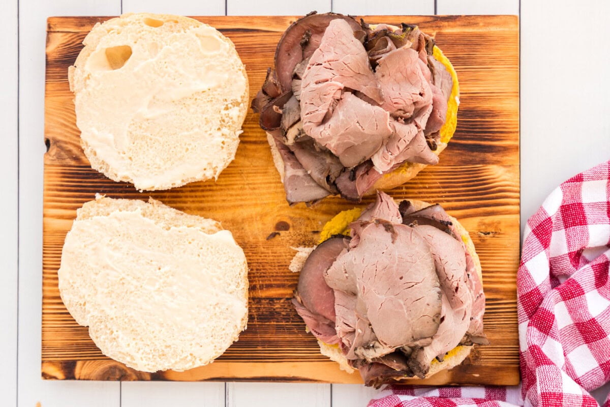 adding roast beef on top of mustard on a bun