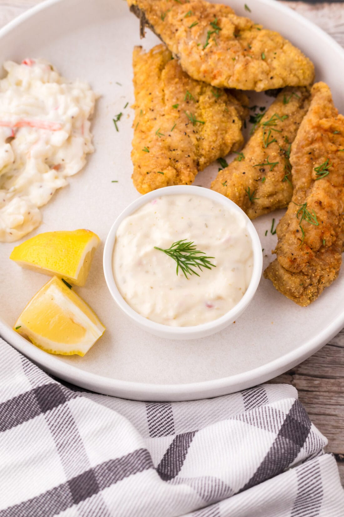 Small bowl of Tartar Sauce on a plate with breaded fish, coleslaw and lemons