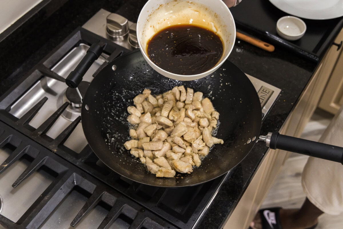 adding teriyaki sauce to wok with chicken