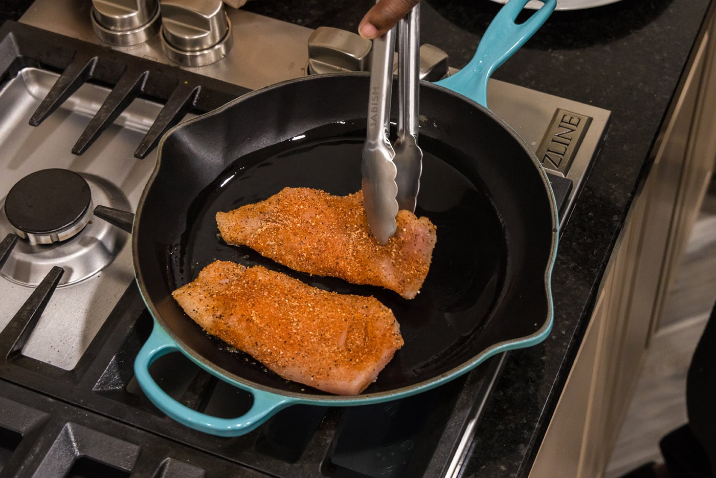tongs adding seasoned chicken breast to skillet