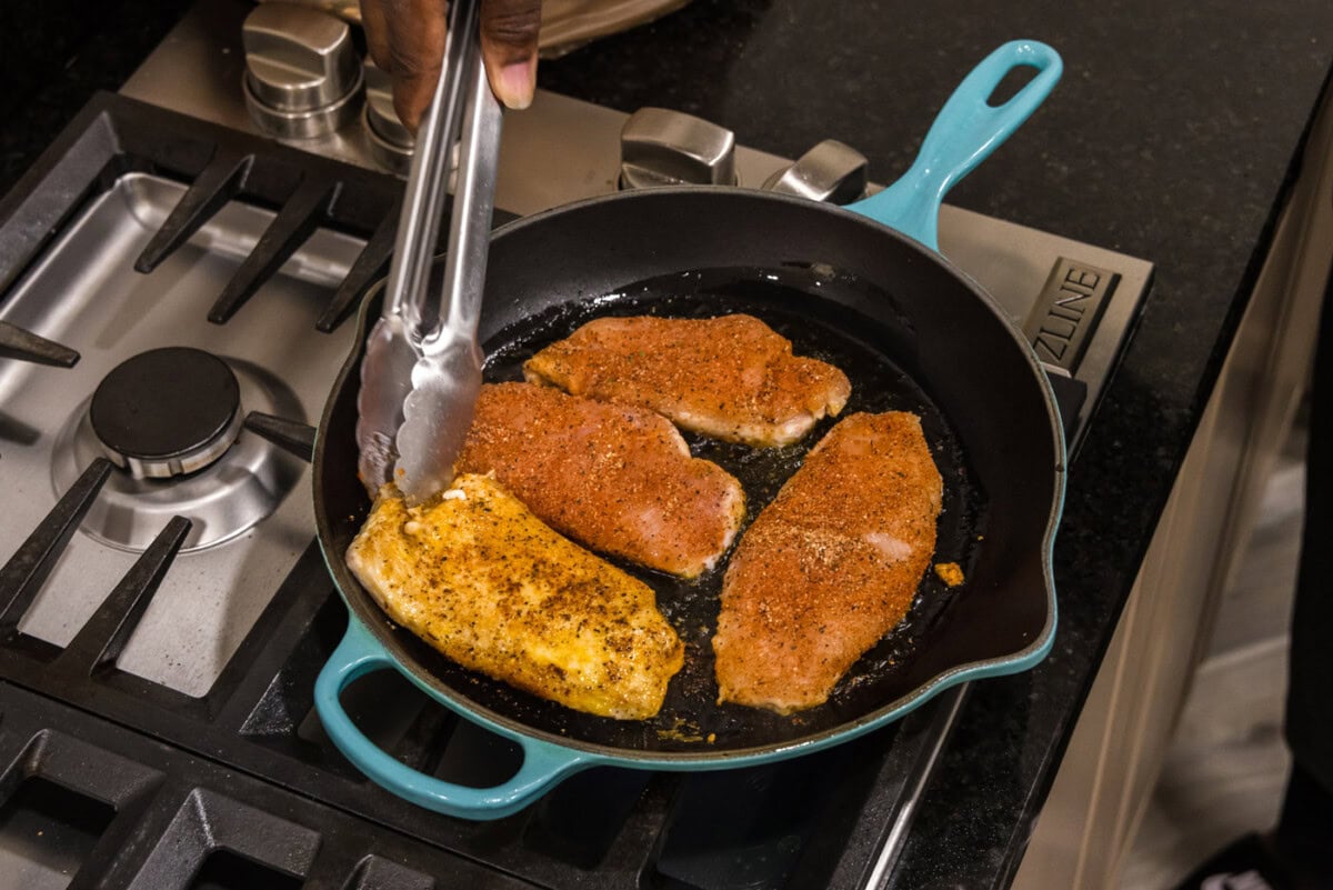 tongs flipping seasoned chicken breasts in a skillet