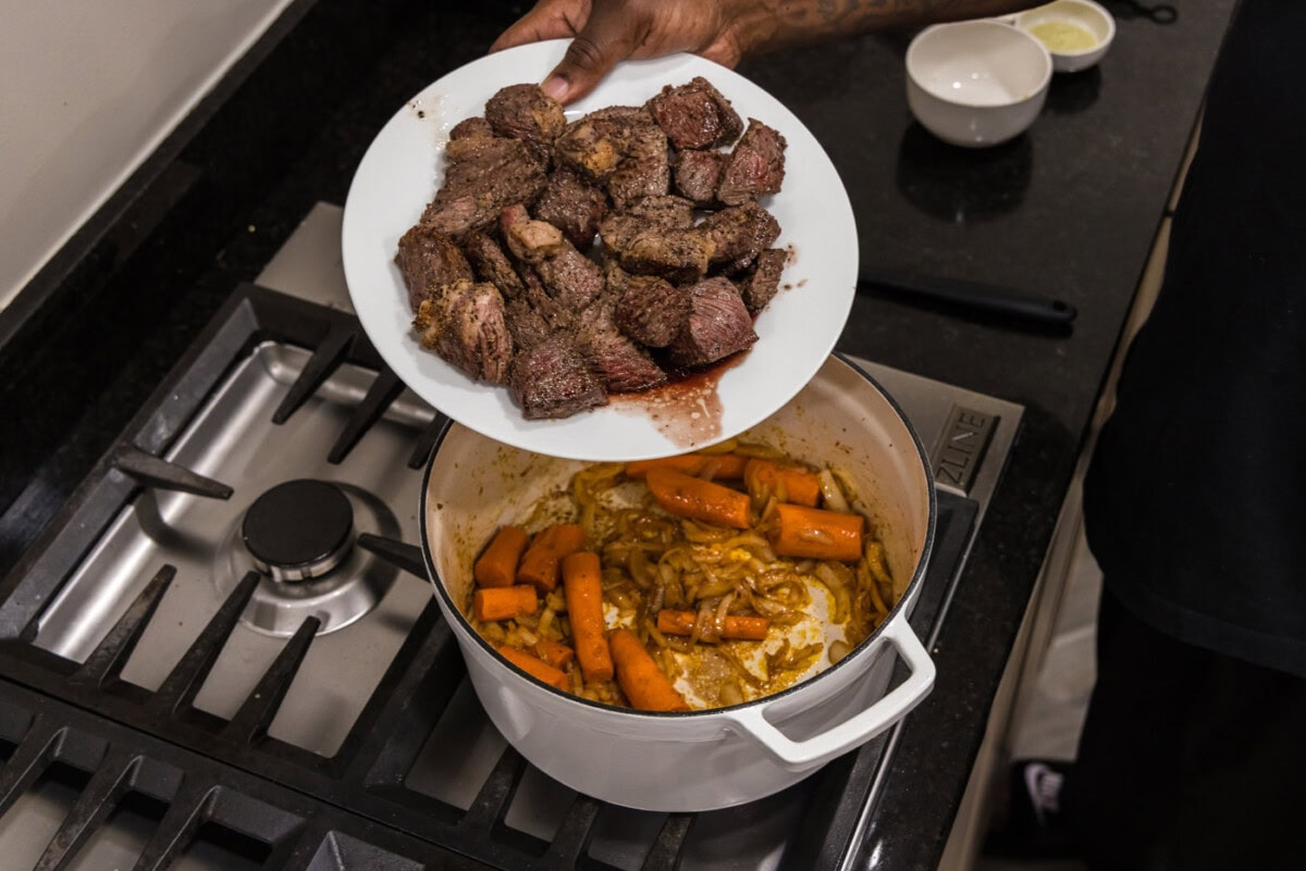 adding beef back to dutch oven with carrots and onions