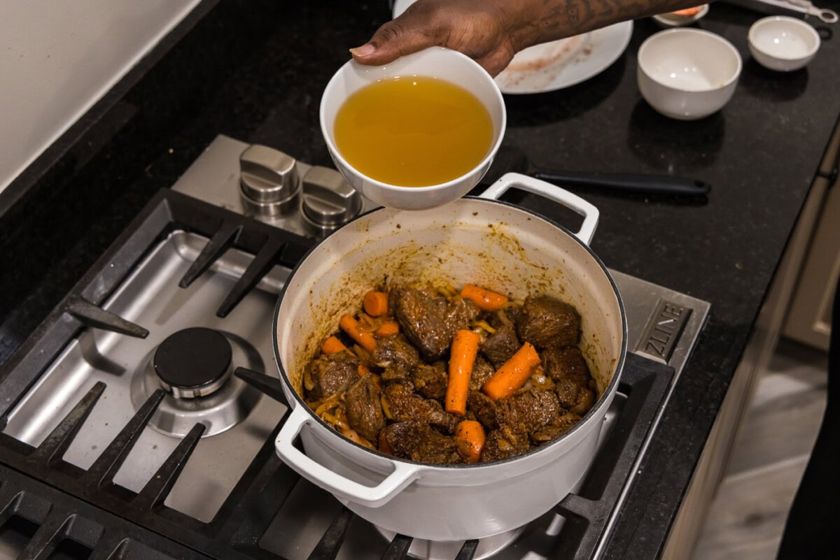 adding chicken stock to braised beef
