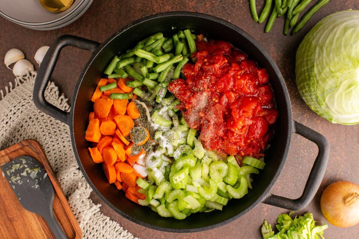 celery, carrot, onion, tomato, and green beans in a soup pot