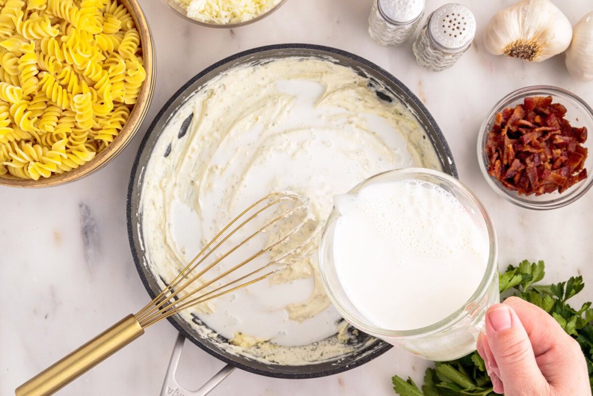 pouring whole milk into skillet with cream cheese