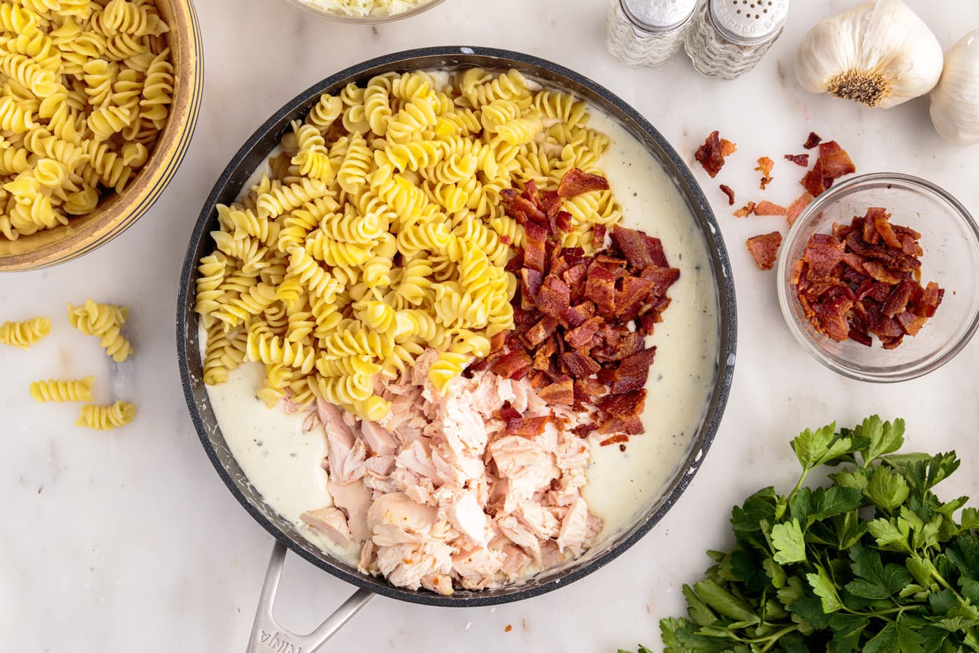 pasta, bacon, and chicken added to cream cheese sauce in a skillet