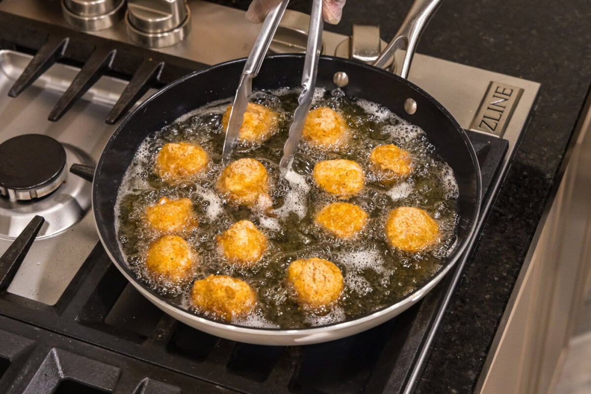 tongs turning scallops in a skillet of oil