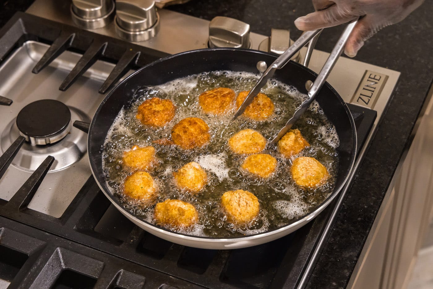 tongs flipping fried scallops in a skillet