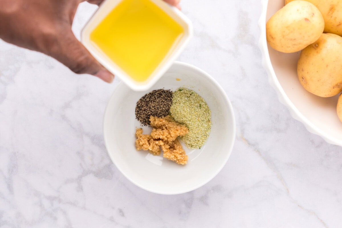 adding olive oil to garlic and seasonings in bowl