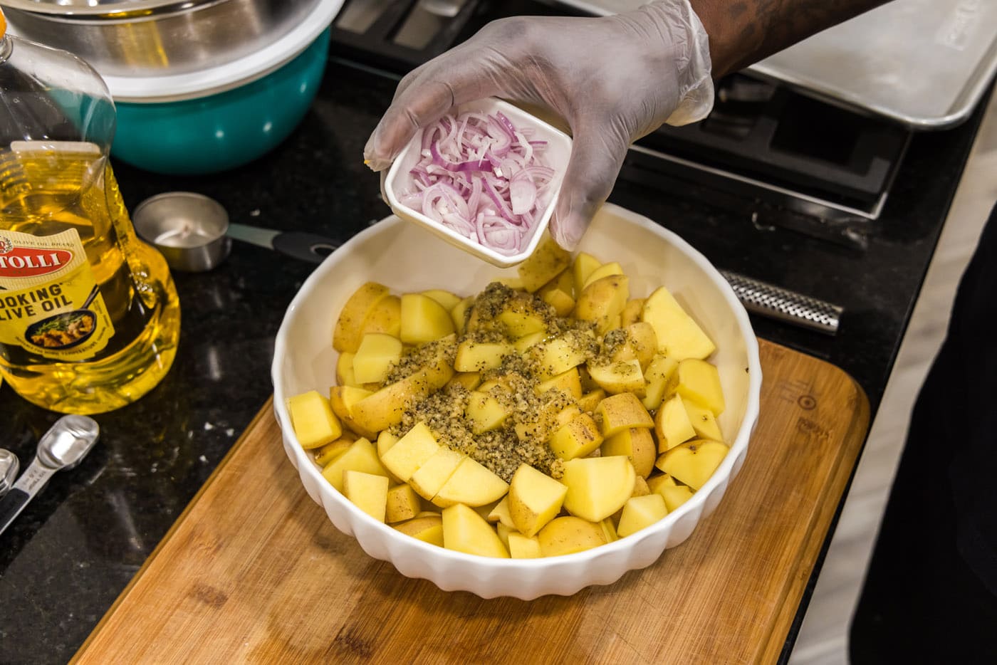 adding shallots to cubed potatoes in a bowl