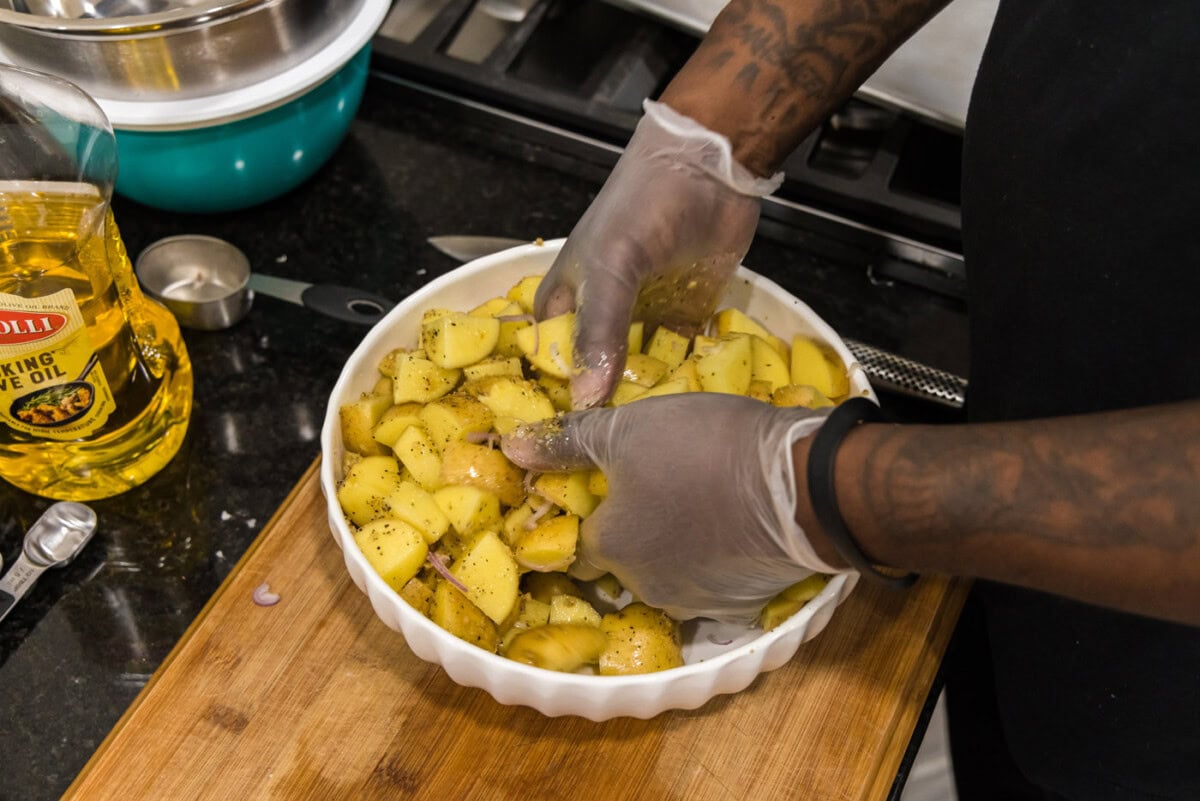 hands mixing cubed potatoes in a bowl