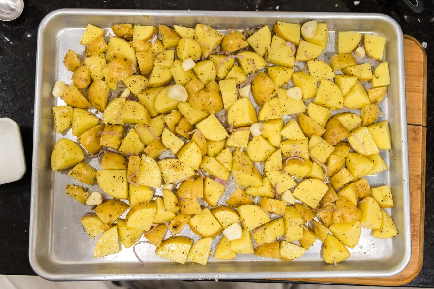 cubed potatoes on a baking sheet with garlic cloves on top