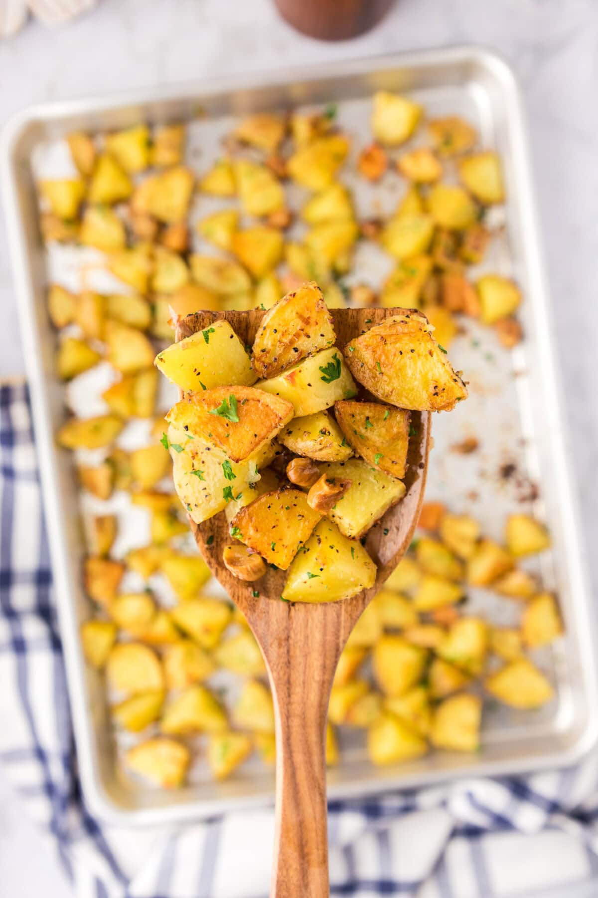 Spatula of Garlic Roasted Potatoes held over a pan of Garlic Roasted Potatoes