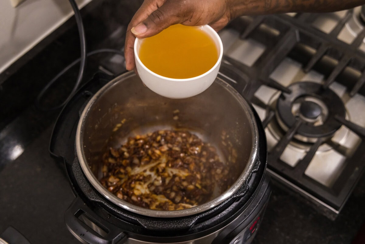 hand holding chicken stock over instant pot with onions