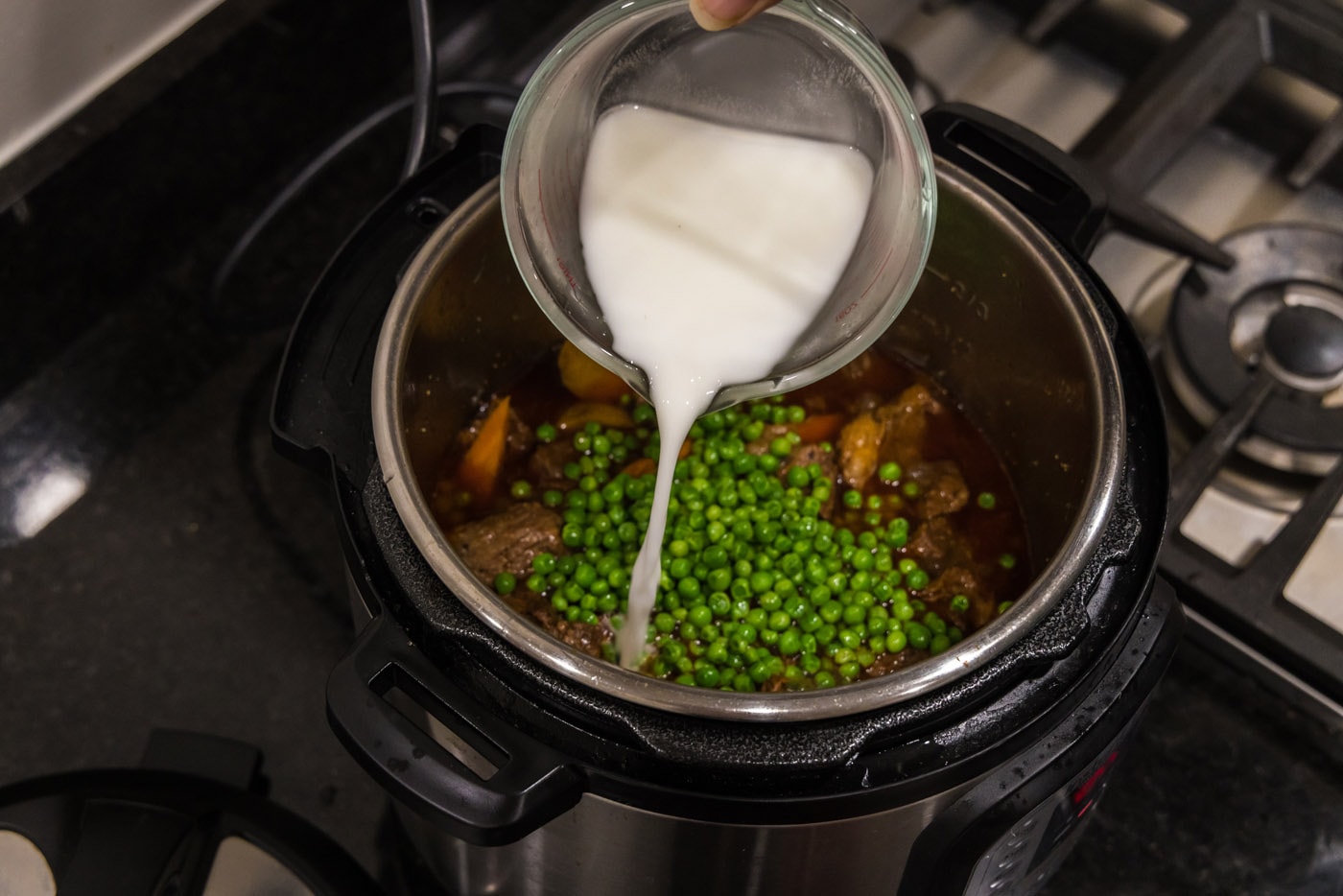 pouring cornstarch slurry into instant pot with peas, beef, potatoes, and carrots