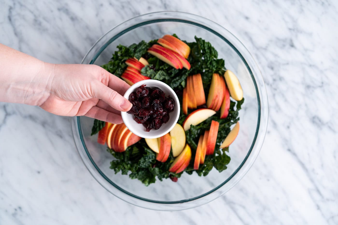 adding craisins to apples and kale in a bowl