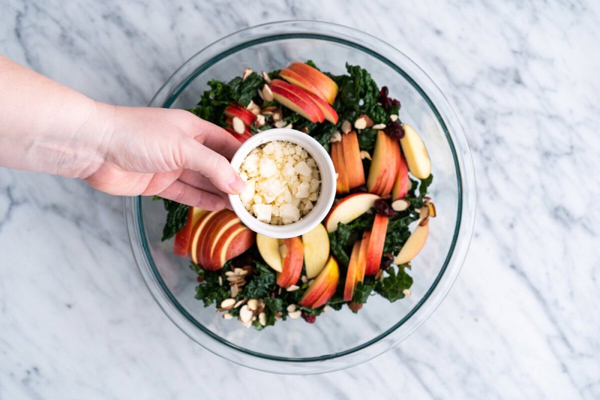 adding crumbled feta to kale salad