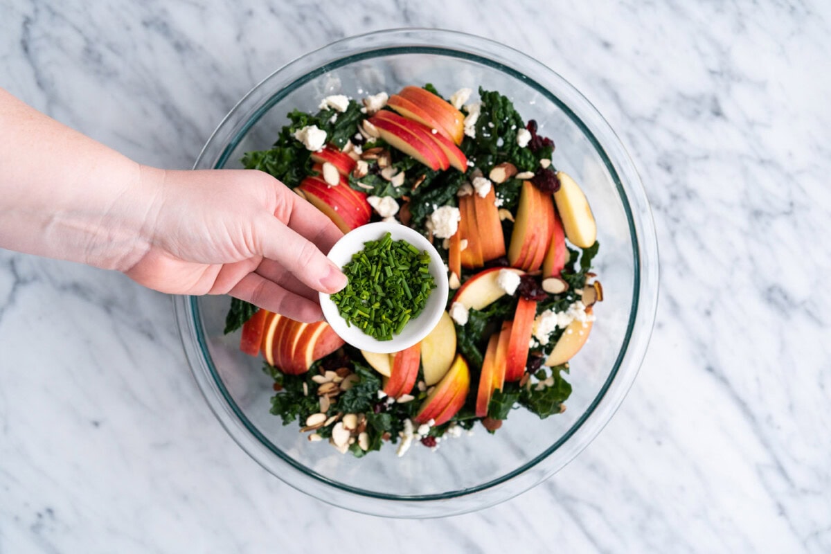 adding chives to kale salad in a bowl