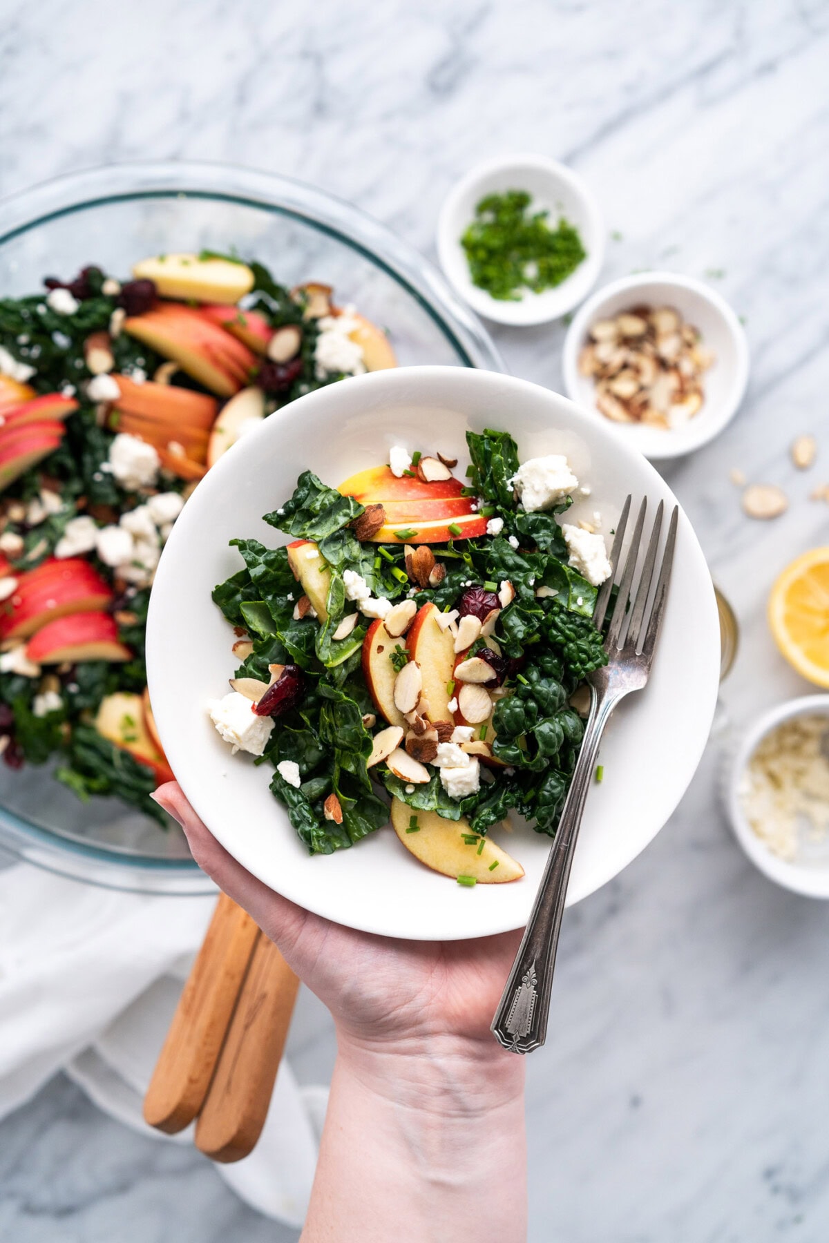 Singe serving of Kale Salad in a bowl being held over the batch of Kale Salad