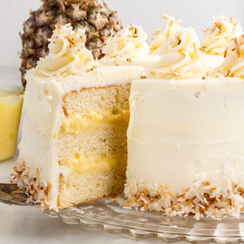 Pineapple Coconut Cake on a cake stand with a slice being removed