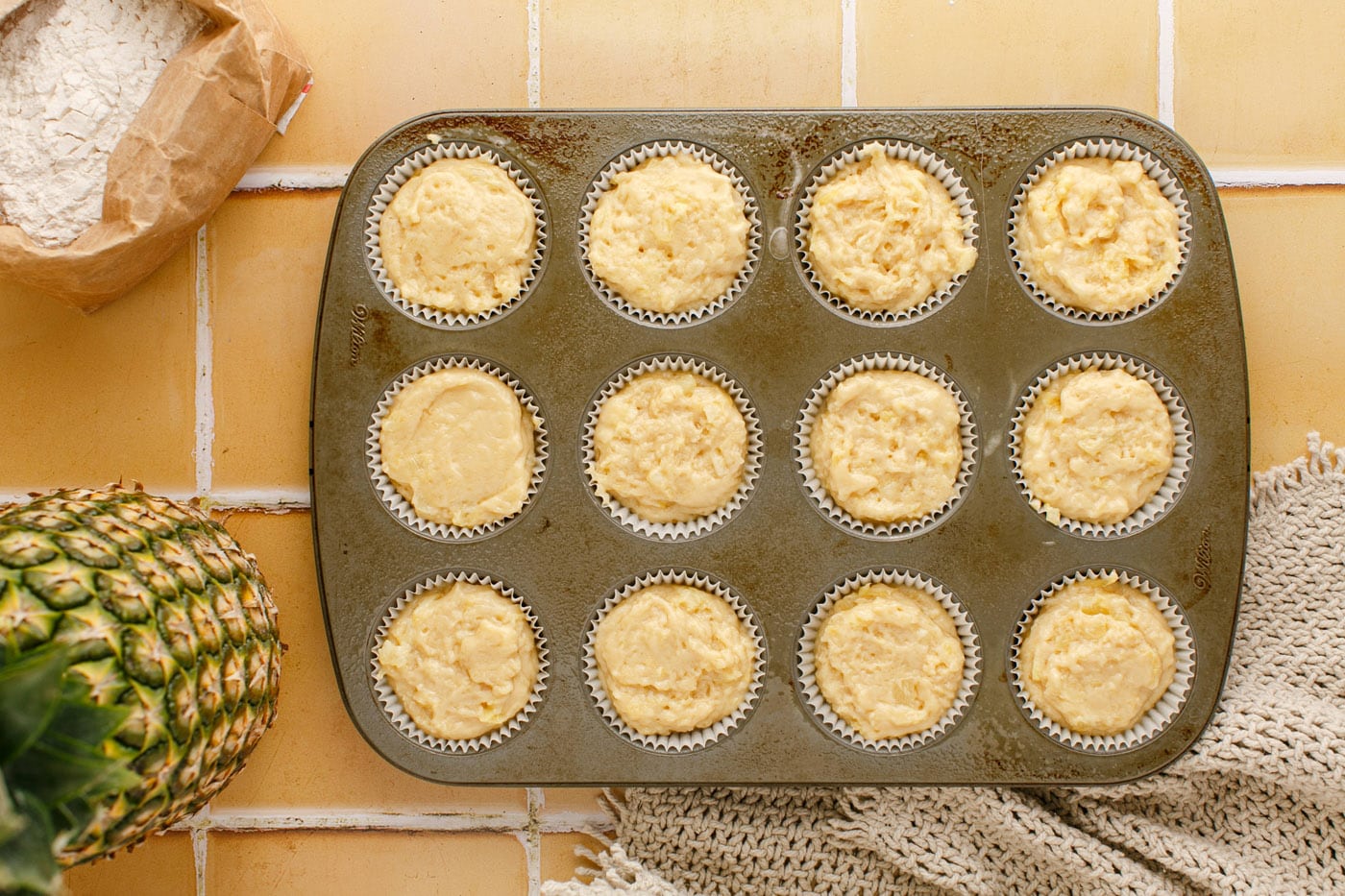 pineapple muffin batter in a muffin pan with liners