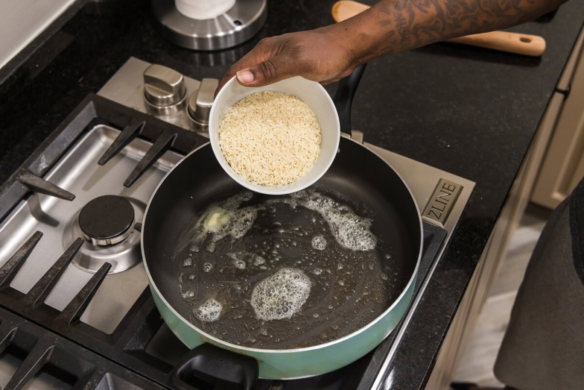 adding rice to skillet with chicken stock