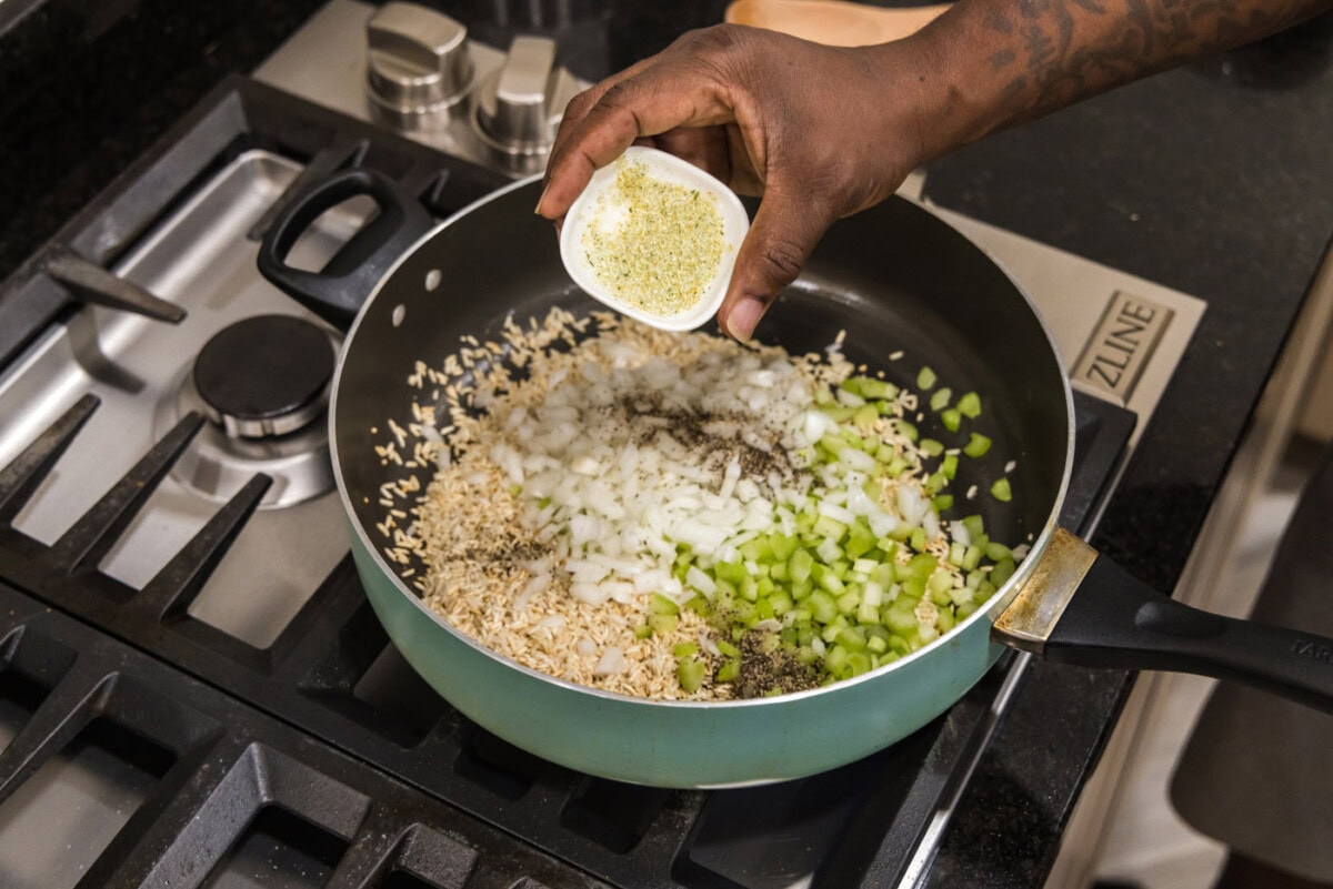 adding garlic salt to celery, onions, rice, and seasonings in a skillet