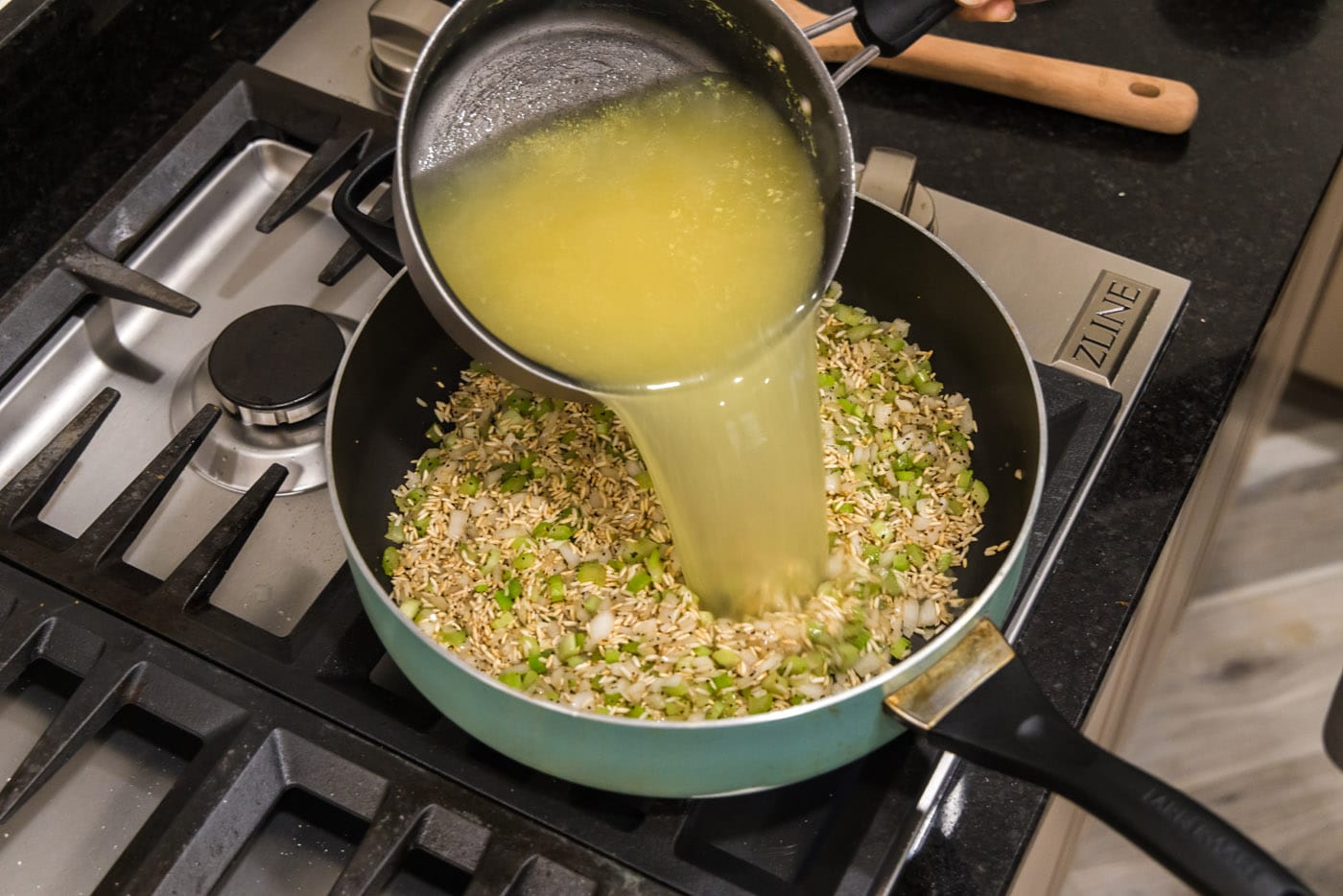 pouring chicken stock and water into rice pilaf in a skillet